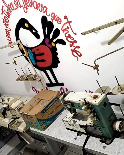 Máquinas de costura industriais do ateliê diante do mural com o pássaro Sankofa