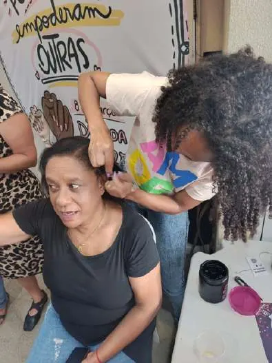 Aluna do curso de beleza atende uma mulher na ação do Dia da Mulher