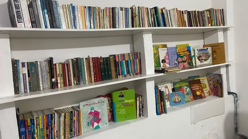 Estantes brancas cheias de livros, com livros infantis de capa colorida na parte de baixo