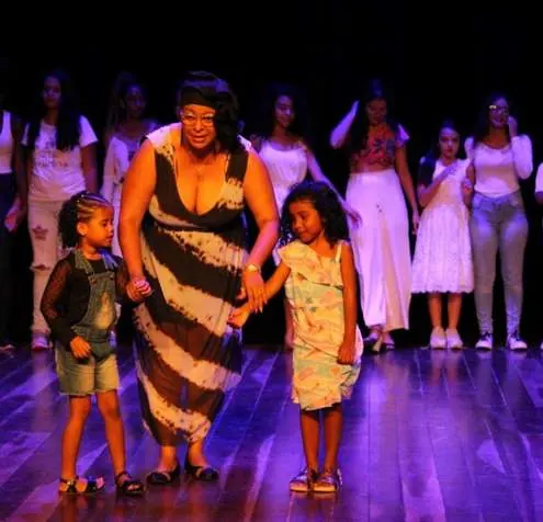 Mulher e duas meninas de mãos dadas no palco do Teatro Municipal de São Gonçalo
