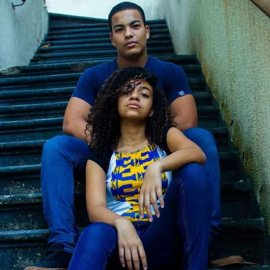Casal de jovens sentado numa escadaria, ela com blusa de estampa africana